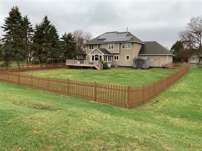 Before image of a large suburban home with a wooden deck and fenced backyard surrounded by green grass and trees in White Bear Lake.