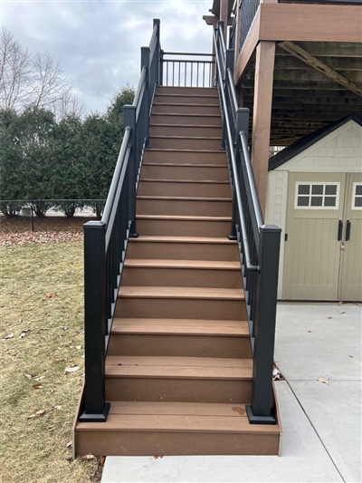 A tall staircase with brown composite steps and black railings, leading up to a raised deck in New Prague.